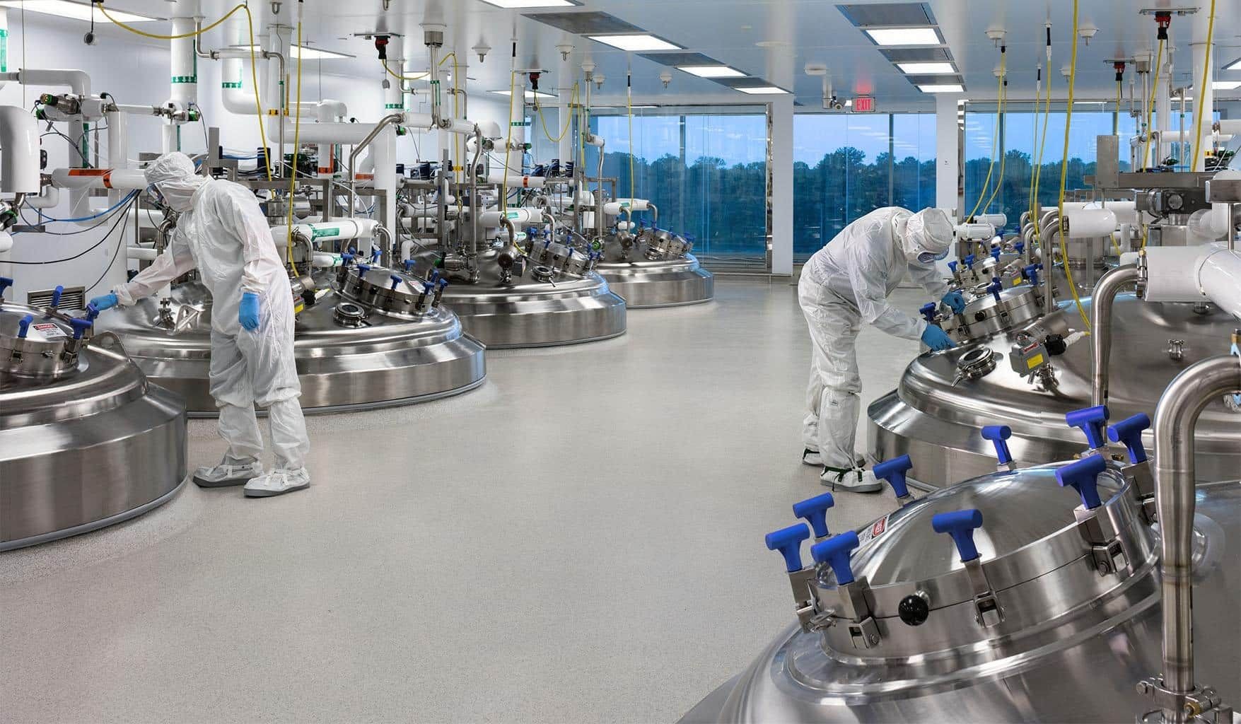 Scientists in protective gear work in a sterile laboratory with large stainless steel equipment.