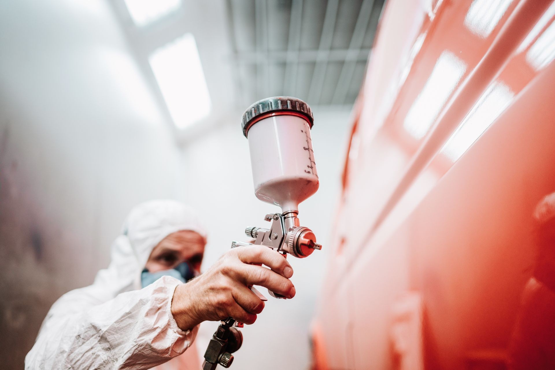 Person in protective gear using a spray gun to paint a vehicle in red.